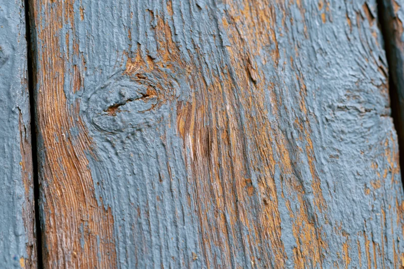 Weathered wooden plank surface filling the frame with peeling blue paint and visible grain