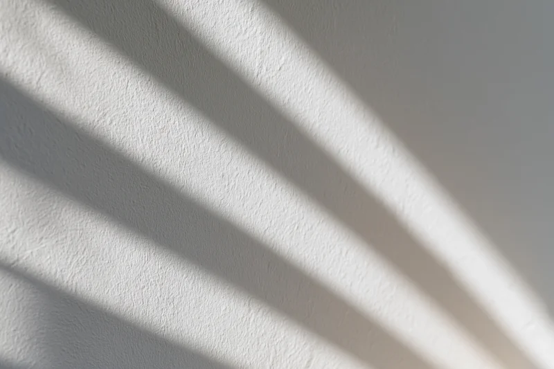 White plaster wall with diagonal light and shadow stripes filling the frame