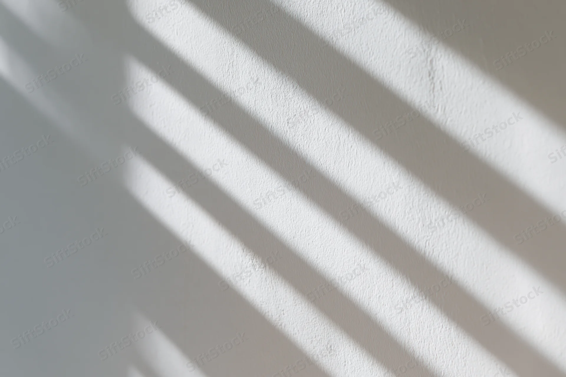 White plaster wall with diagonal light and shadow stripes from window blinds