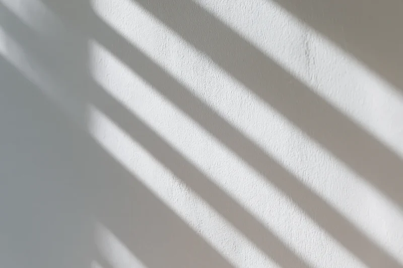 White plaster wall with diagonal light and shadow stripes from window blinds