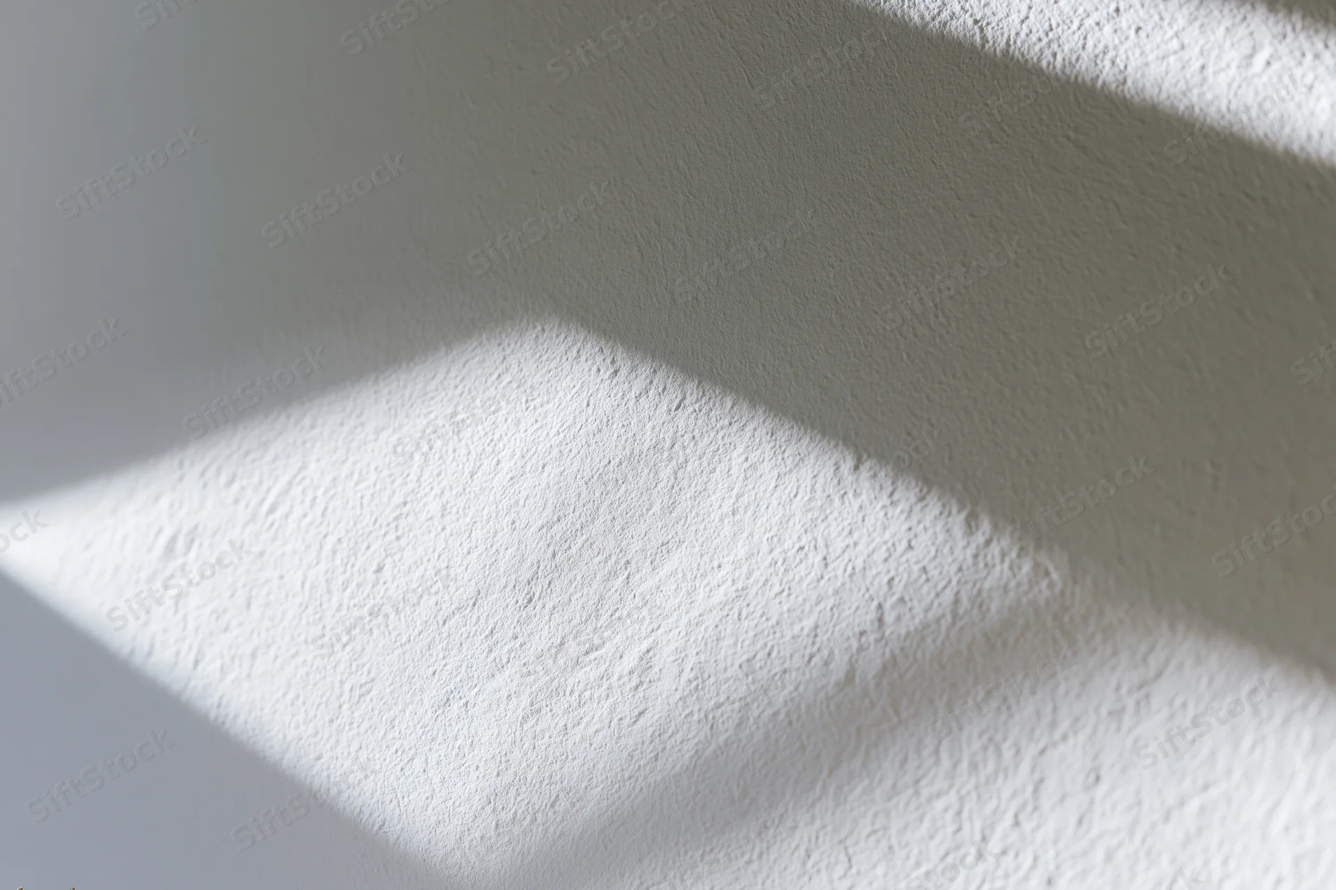 White textured plaster wall with soft diagonal sunlight and shadow pattern