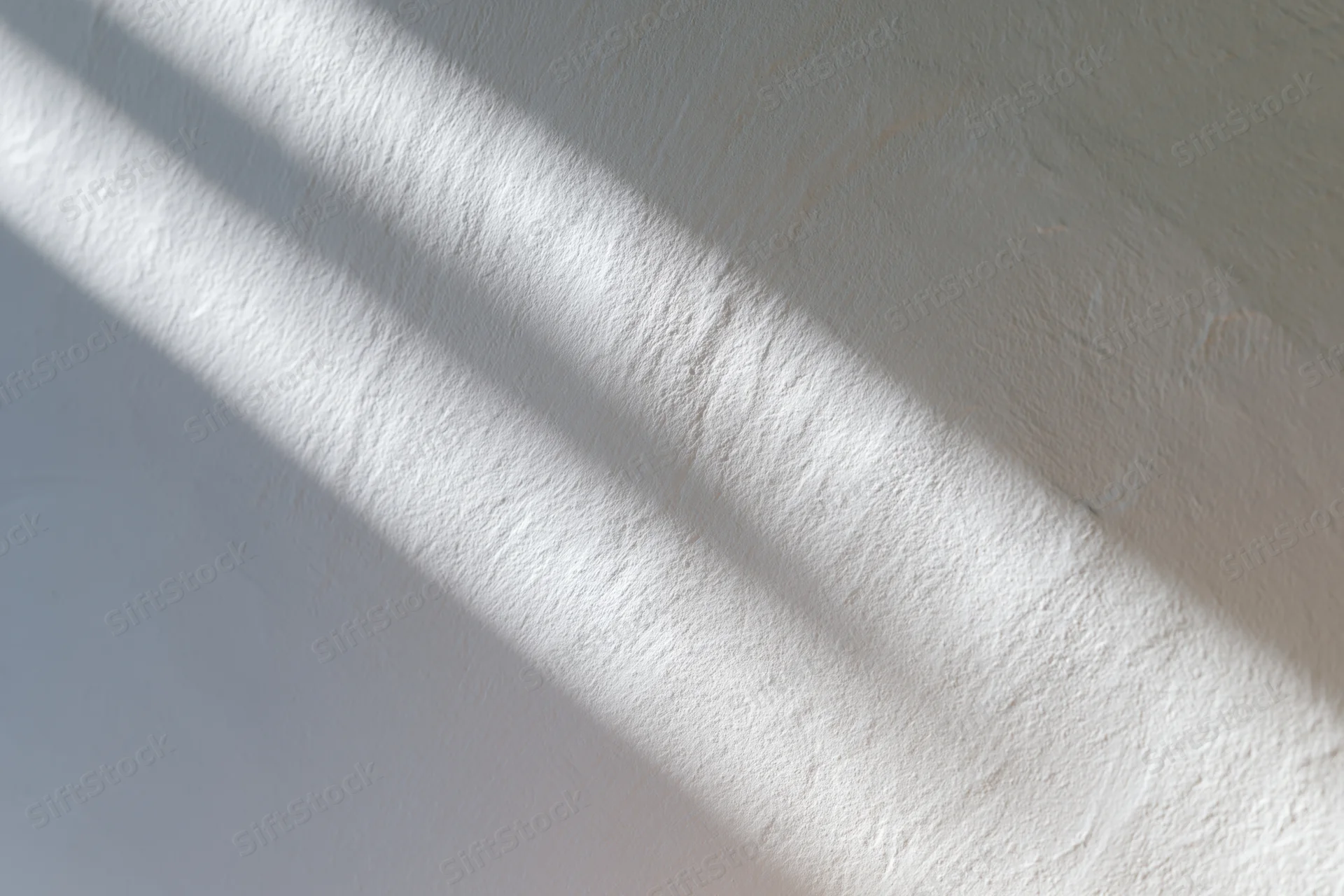 White textured plaster wall with soft diagonal light and shadow from a window
