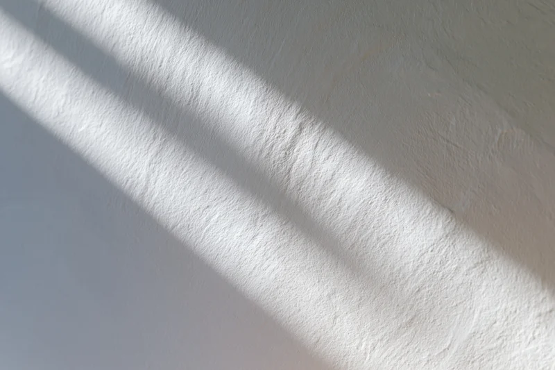 White textured plaster wall with soft diagonal light and shadow from a window
