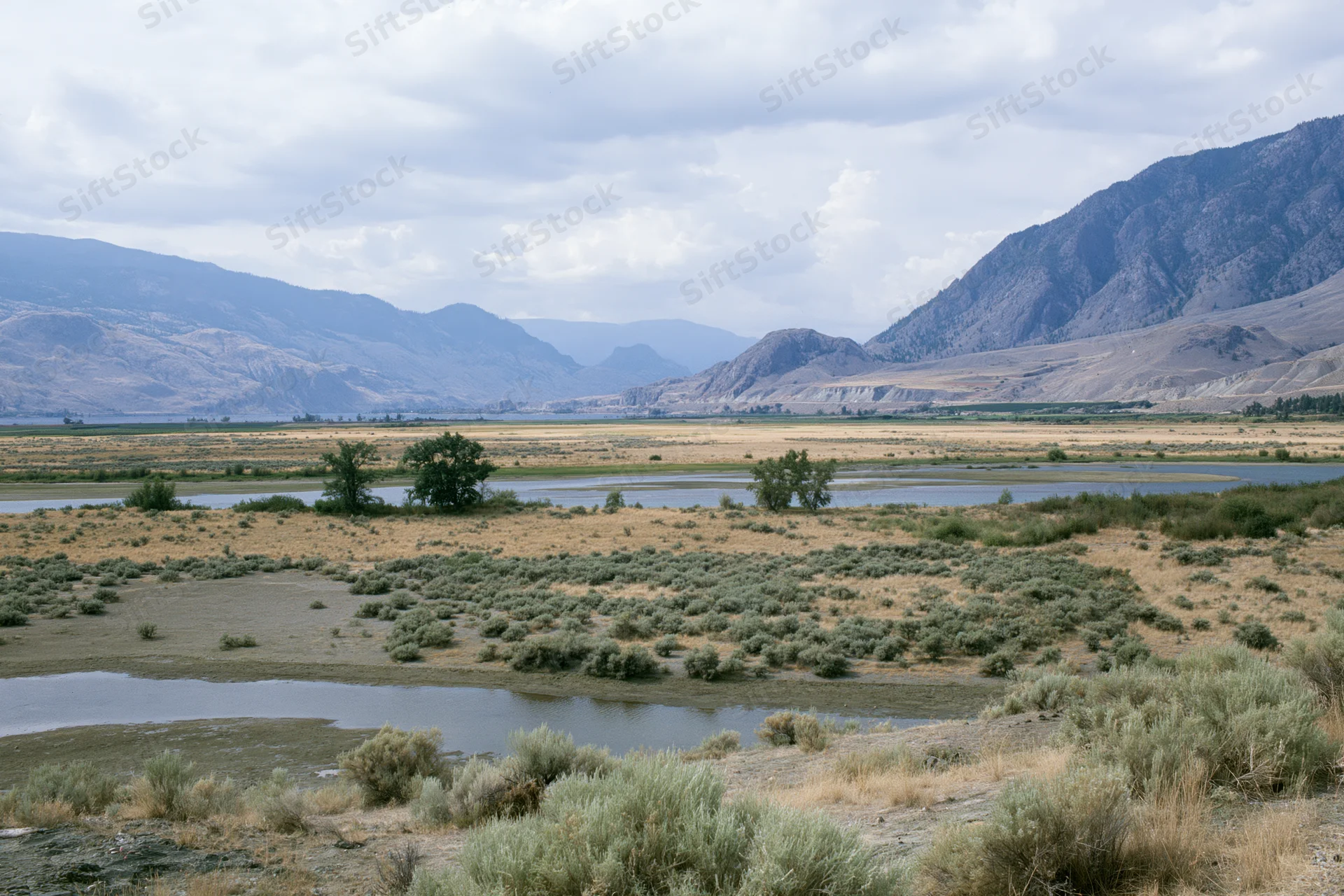 Wide view of a river winding through a dry valley with rocky mountains in the background