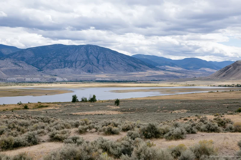 Wide view of a river winding through a sagebrush valley with rocky mountains in the background under cloudy sky