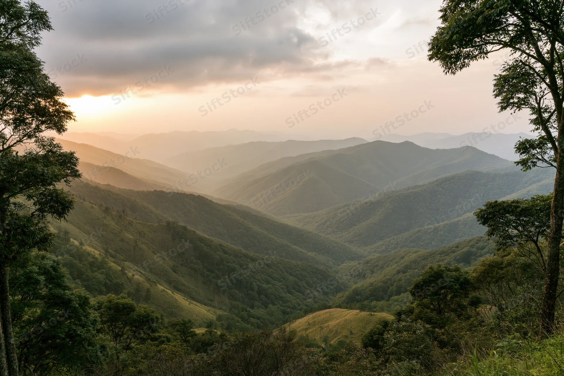 Layered green mountain ridges receding into the distance under a cloudy sunset sky