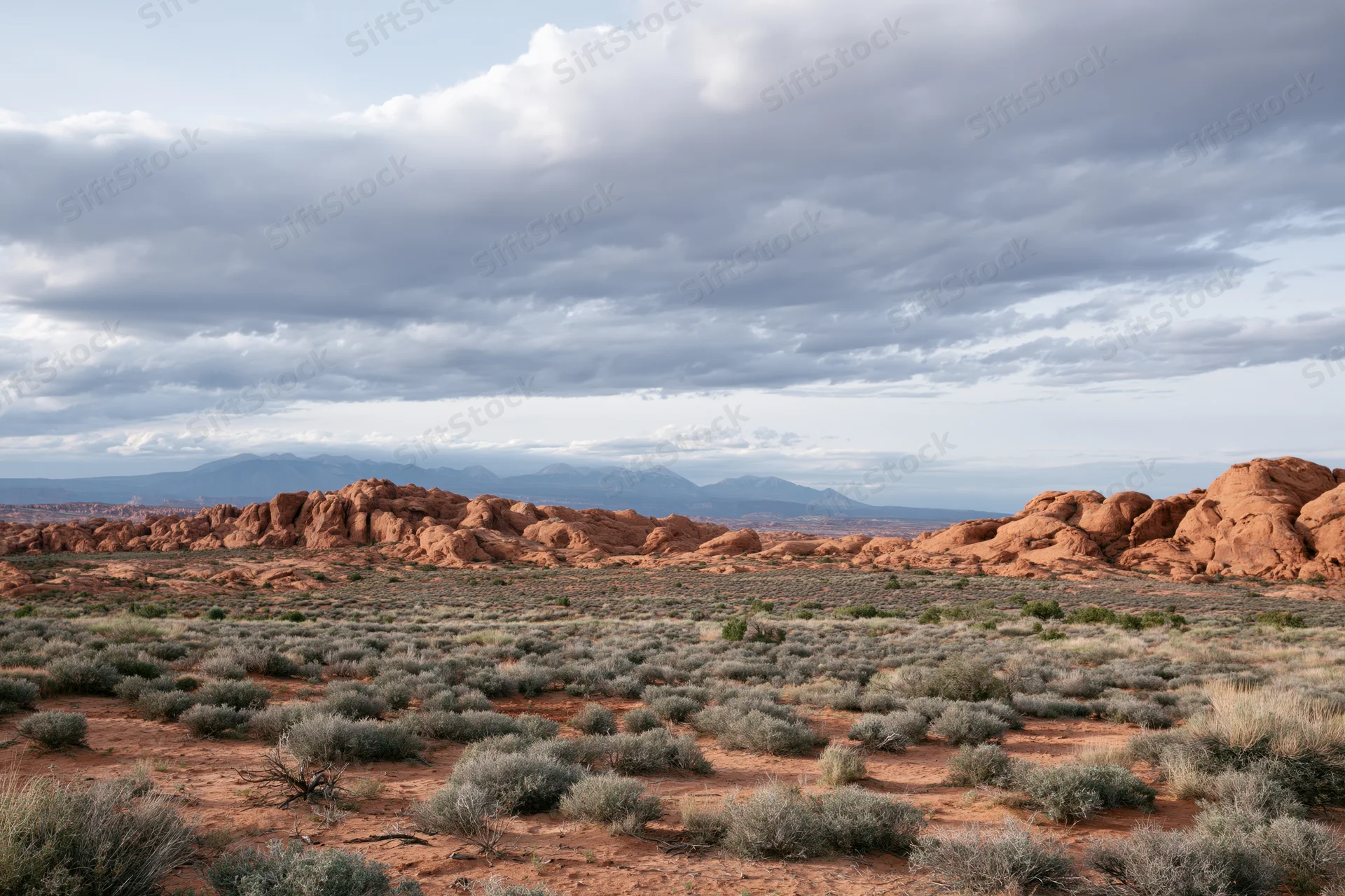 Red sandstone rock formations rising from desert scrub under cloudy sky