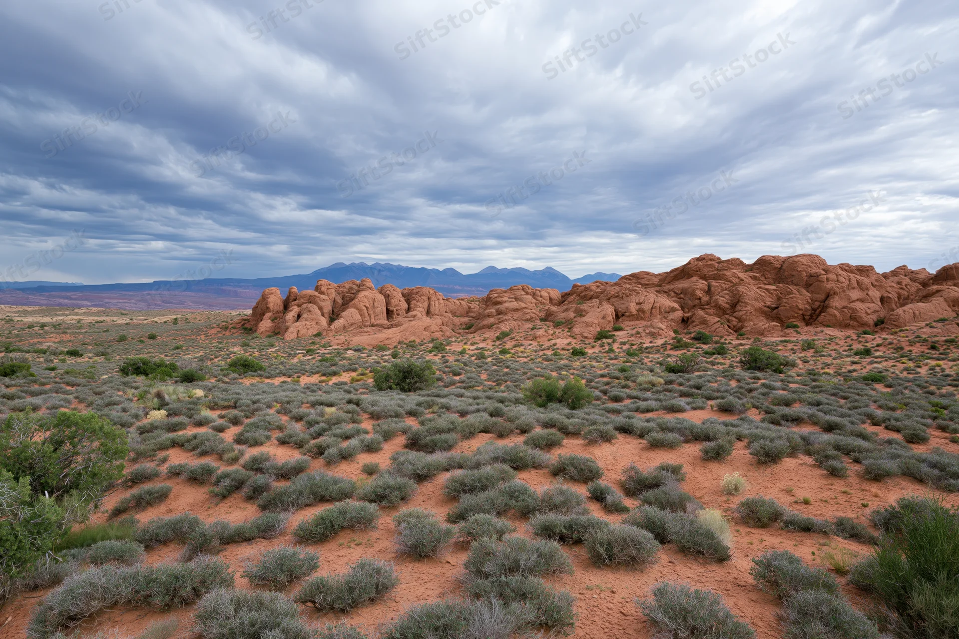 Red sandstone rock formations rising from desert landscape under cloudy sky