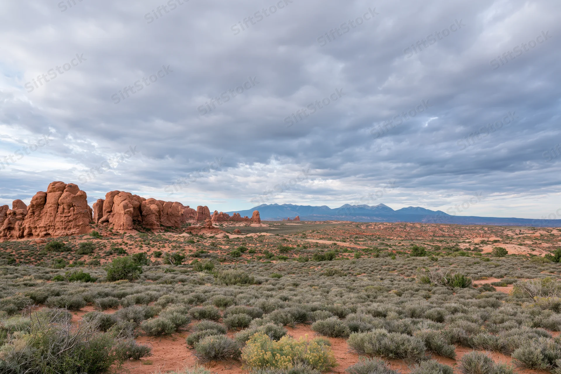 Red sandstone rock formations rising from desert landscape under cloudy sky
