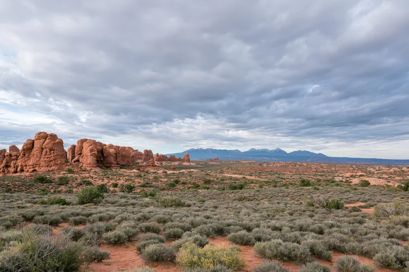 Red sandstone rock formations rising from desert landscape under cloudy sky