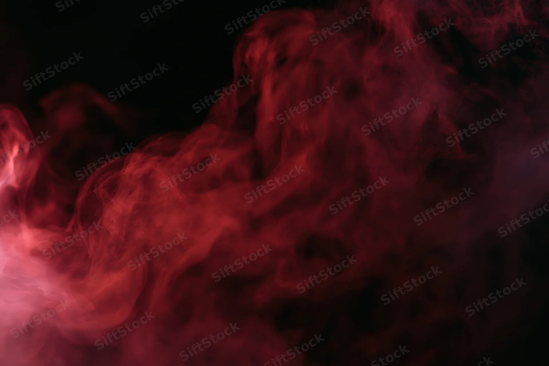 Red smoke swirling and drifting against a black background