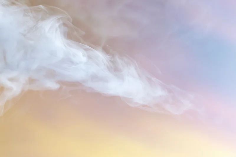 Wispy white smoke tendrils drifting and curling against a soft pastel sky background