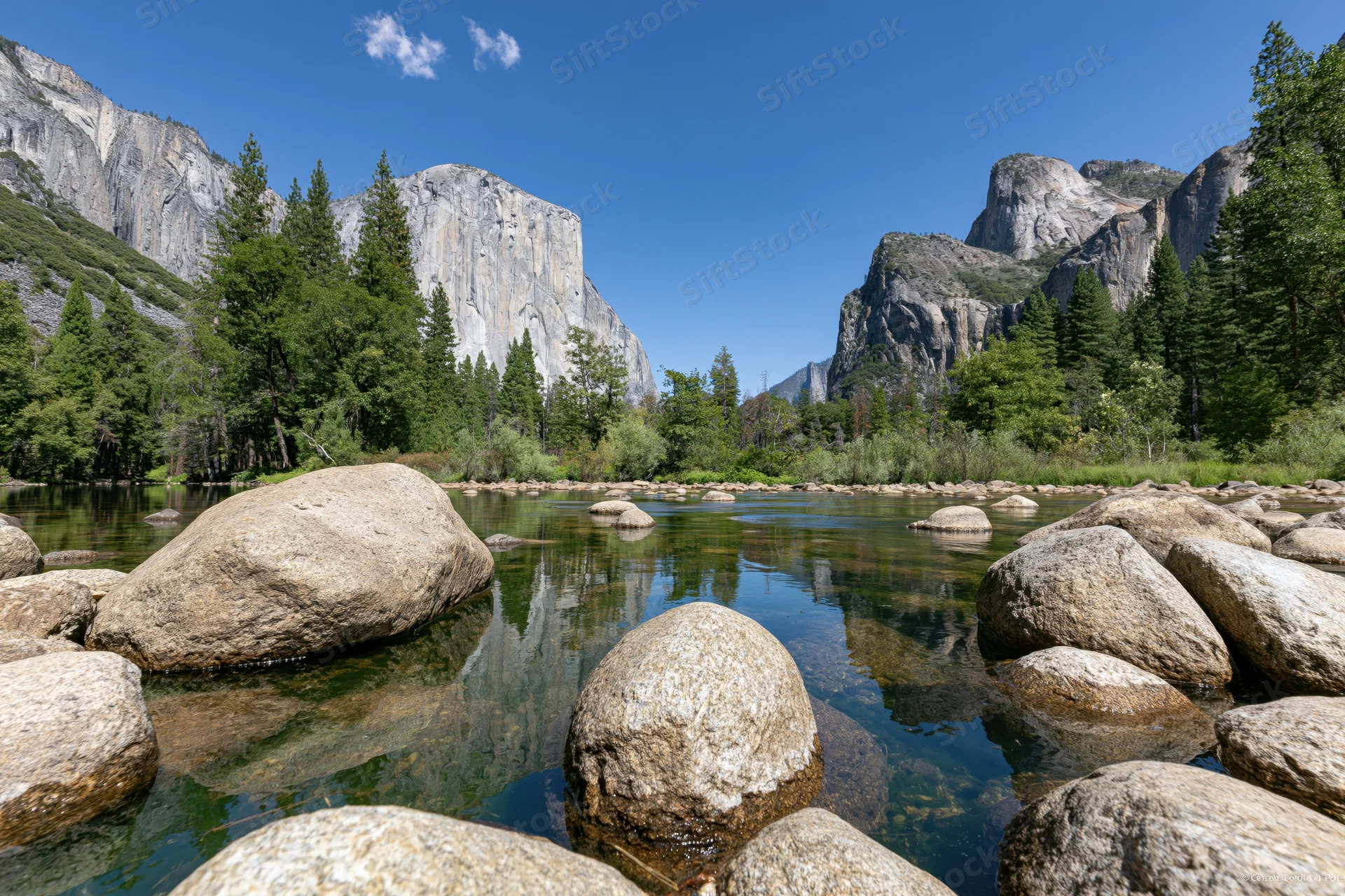 River flowing through yosemite valley with granite cliffs and pine trees reflected in calm water