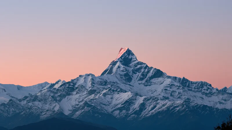 Snow-covered mountain peak at dawn with pink sky and rugged ridges in the Himalayas