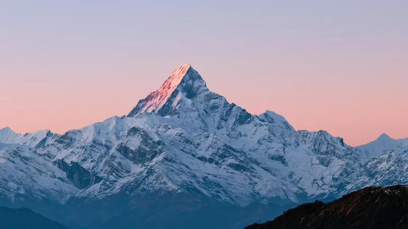 Snow-covered mountain peak glowing at sunrise with alpenglow against a pastel sky