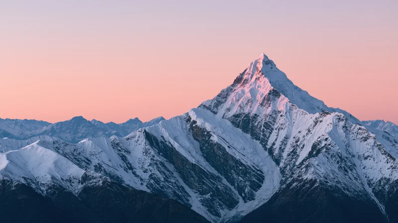 Snow-covered mountain peak rising above ridges at dawn with pink sky above