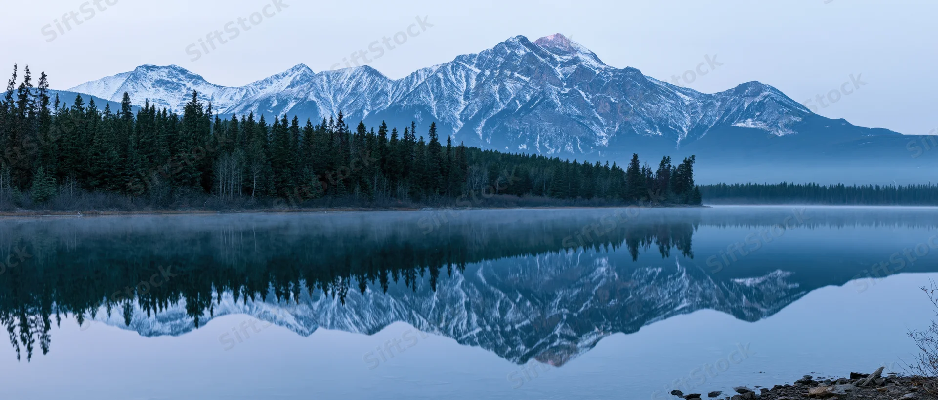Snow-capped mountain range reflected in calm lake surrounded by evergreen forest