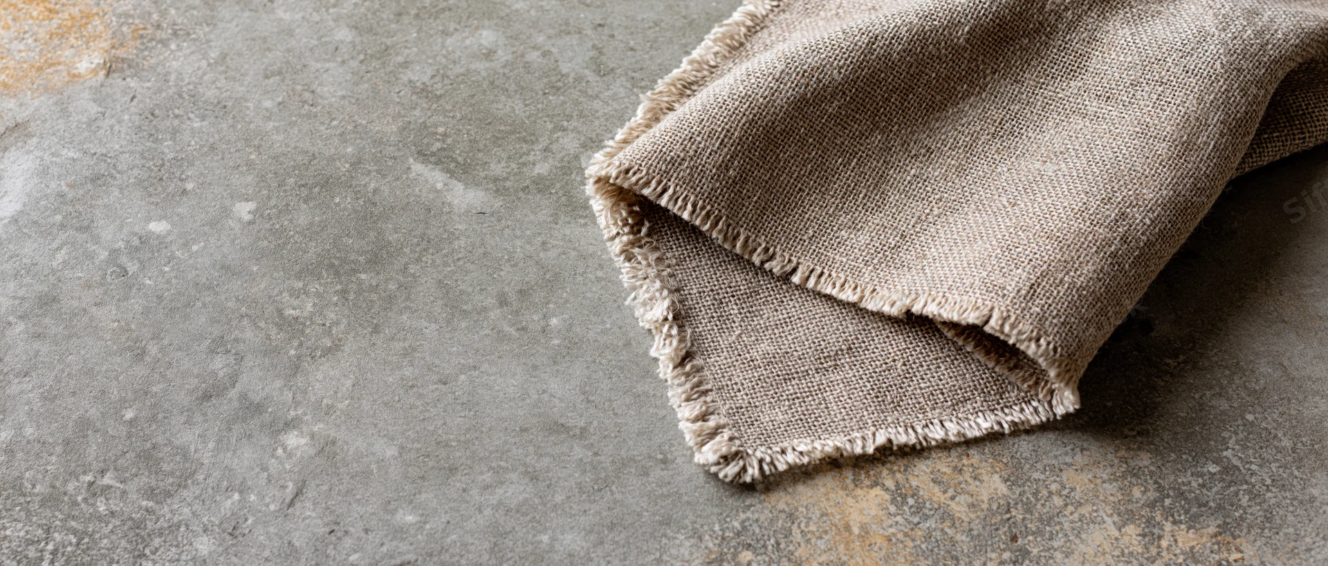 Folded linen fabric with frayed edges resting on a textured concrete surface