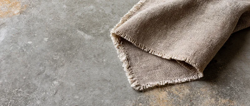 Folded linen fabric with frayed edges resting on a textured concrete surface
