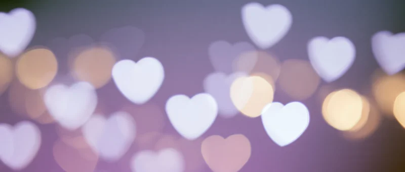 Blurred heart-shaped lights in soft purple and warm tones creating a romantic bokeh background