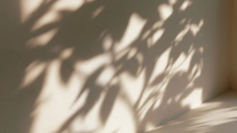 Leaf shadows cast on a beige interior wall in a corner of a room