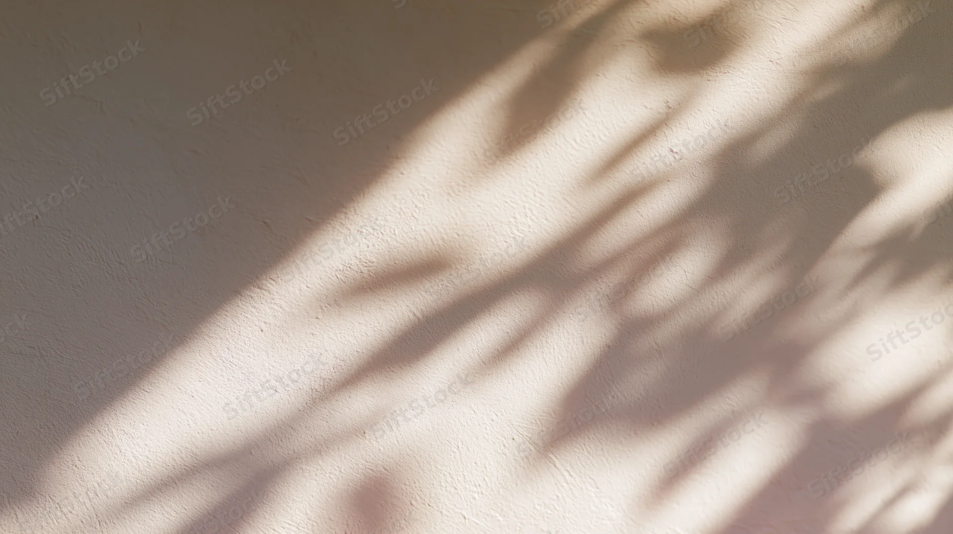 Dappled shadows of leaves cast on a textured beige wall in natural sunlight