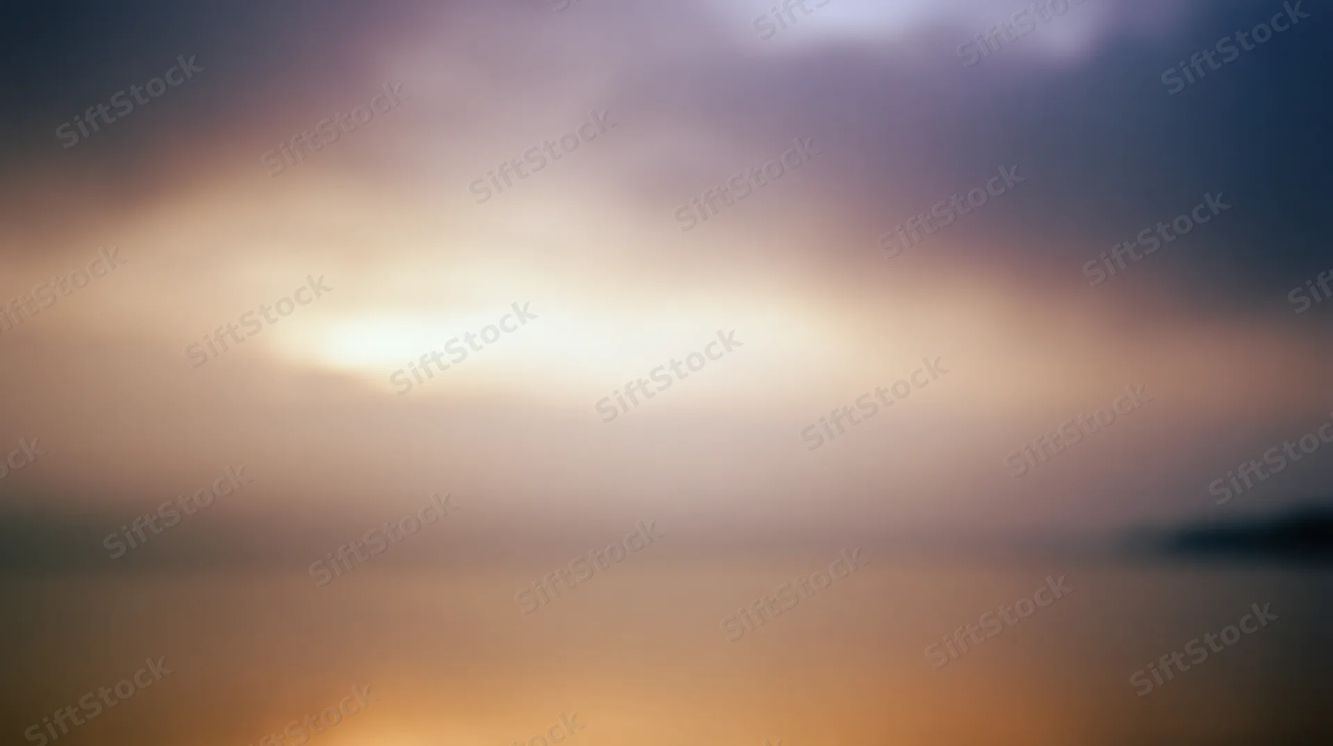 Blurred sunset over calm water with soft clouds and golden light at dusk