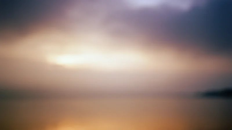 Blurred sunset over calm water with soft clouds and golden light at dusk