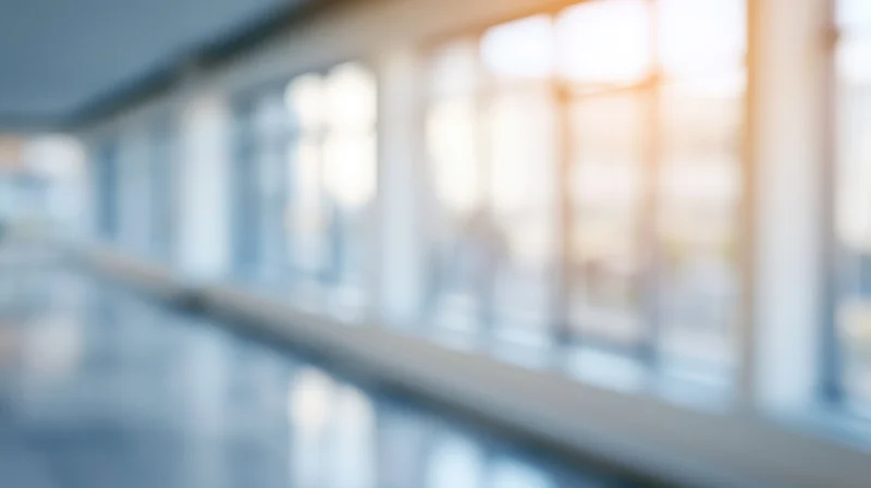 Blurred interior hallway with windows and warm sunlight streaming through, showing modern office building corridor