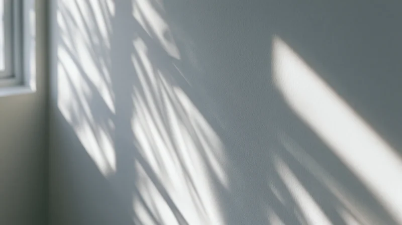 Sunlight filtering through blinds casting striped shadows on a gray wall in a quiet room