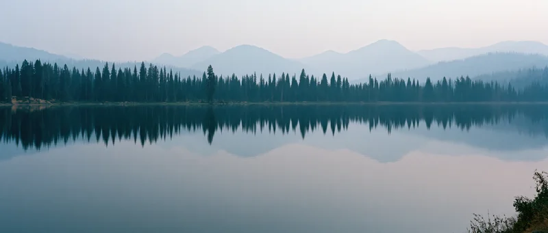 Calm lake reflecting forested mountains at dusk