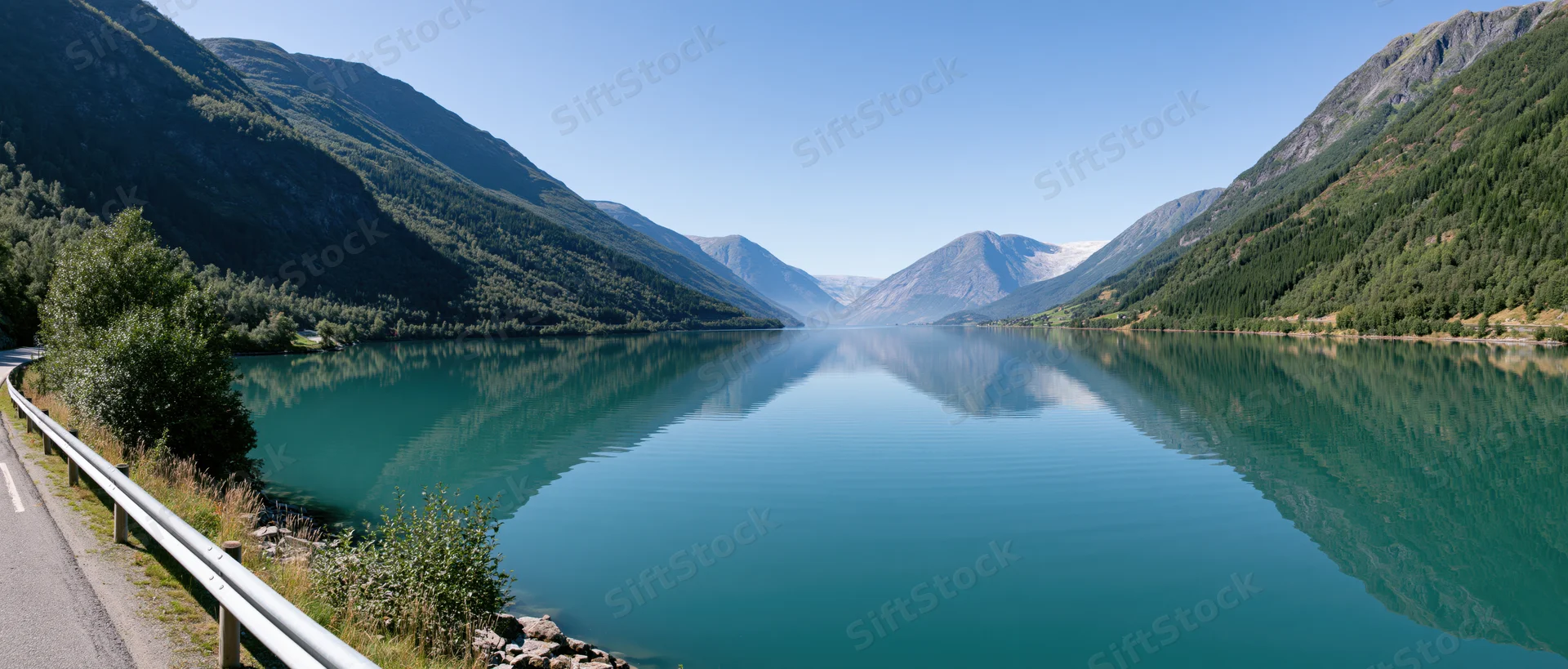 Calm turquoise lake reflecting mountains and forest along a winding road in a fjord valley