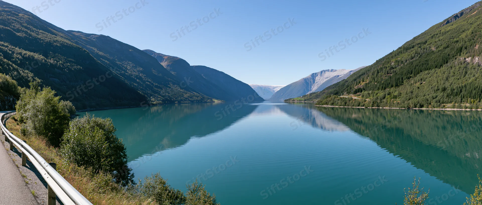 Calm turquoise lake reflecting surrounding mountains and forest along a winding road in a Norwegian fjord valley