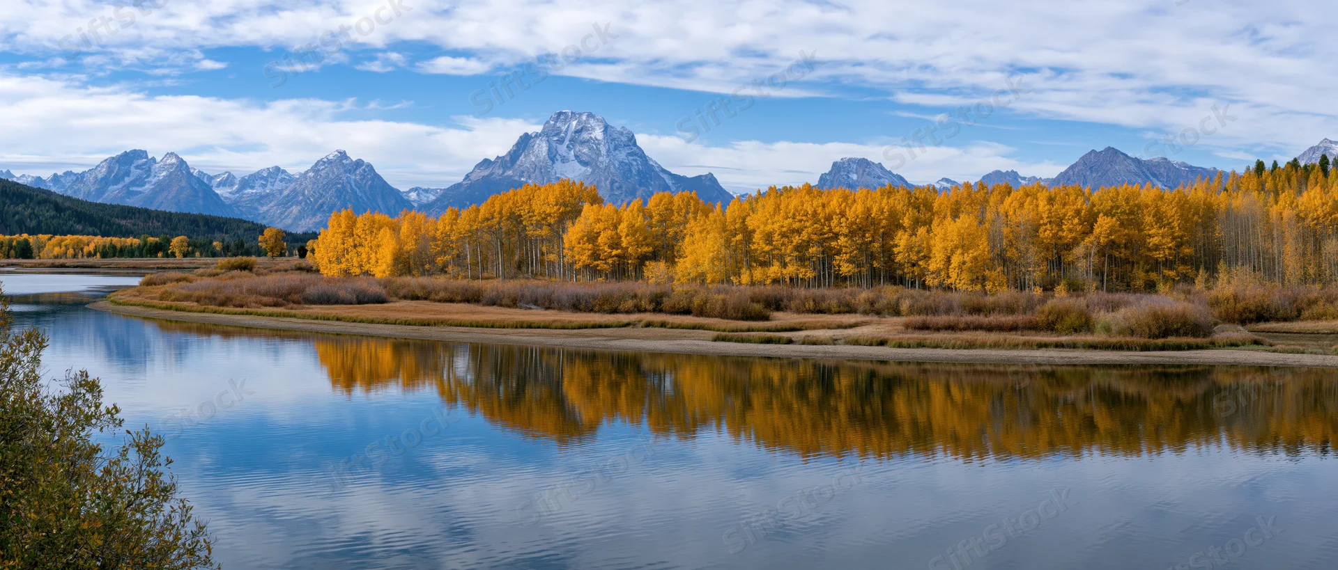 Golden aspen trees lining a calm river reflecting mountains under a blue sky in autumn