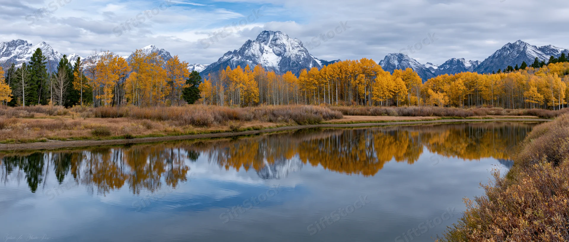 Autumn aspen trees reflecting in calm river below snow-capped mountains in national park