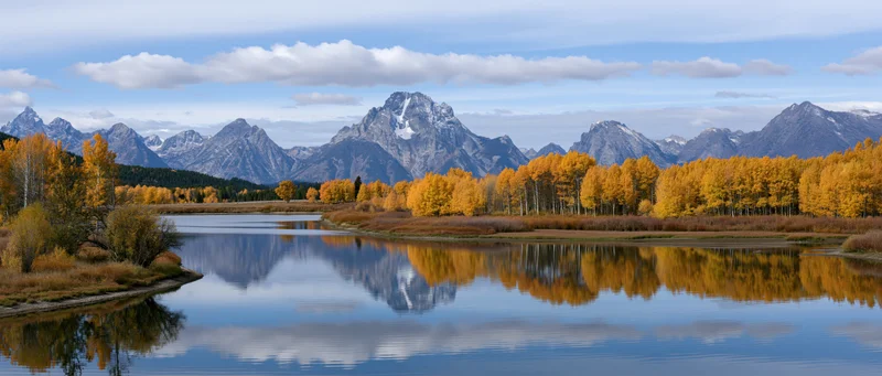 Autumn aspen trees reflecting in calm river below snow-capped mountains in valley