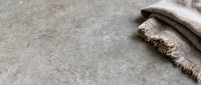 Folded linen textile with frayed edges resting on a textured concrete surface