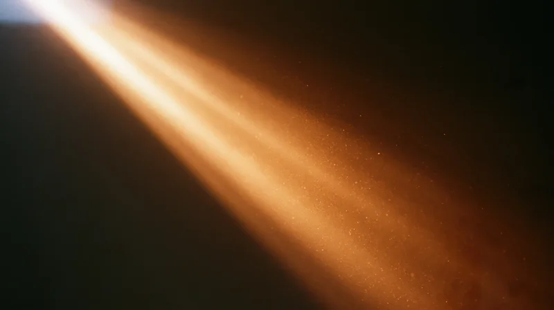 Golden sunbeam cutting through dust particles in a dark room, creating a glowing path of light
