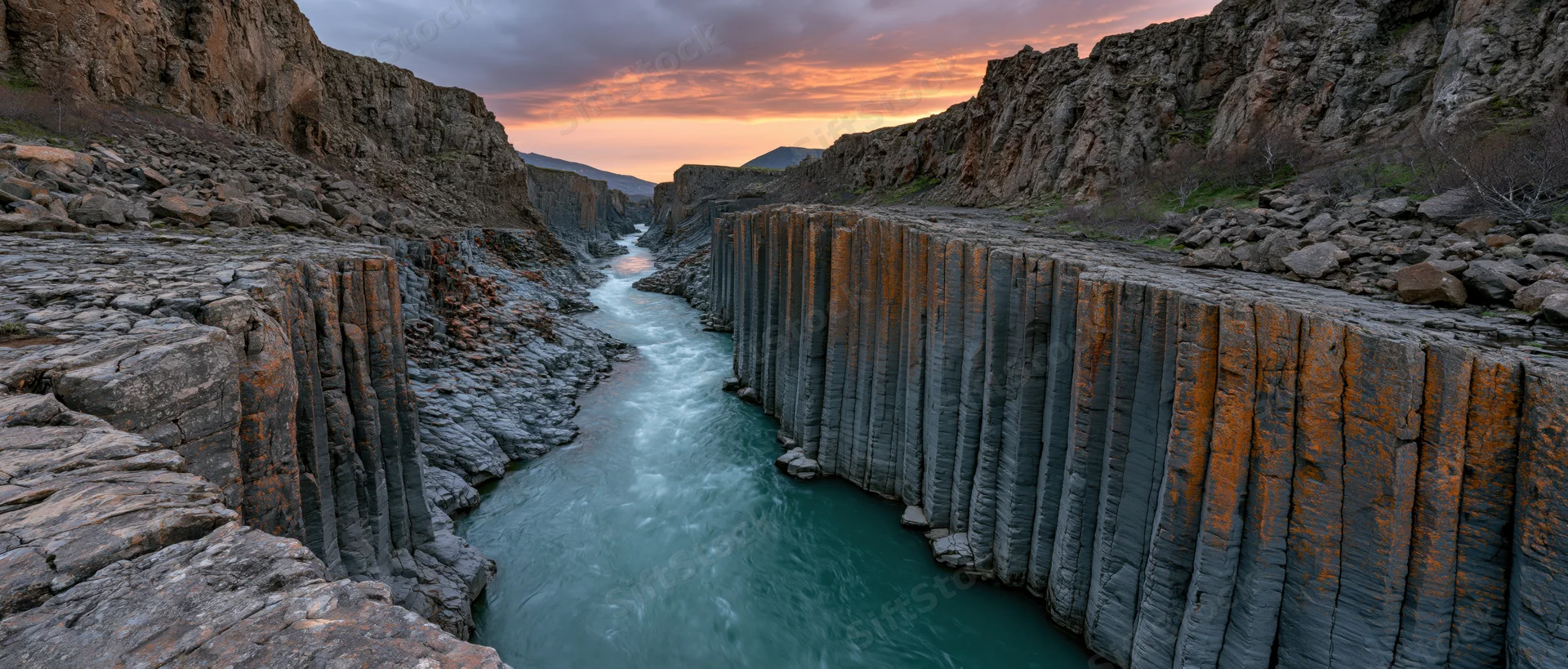 Turquoise river flowing through basalt columns in a narrow canyon at sunset