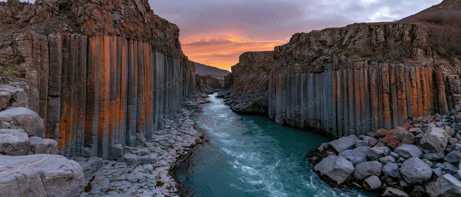 Turquoise river flowing through basalt columns in a canyon at sunset
