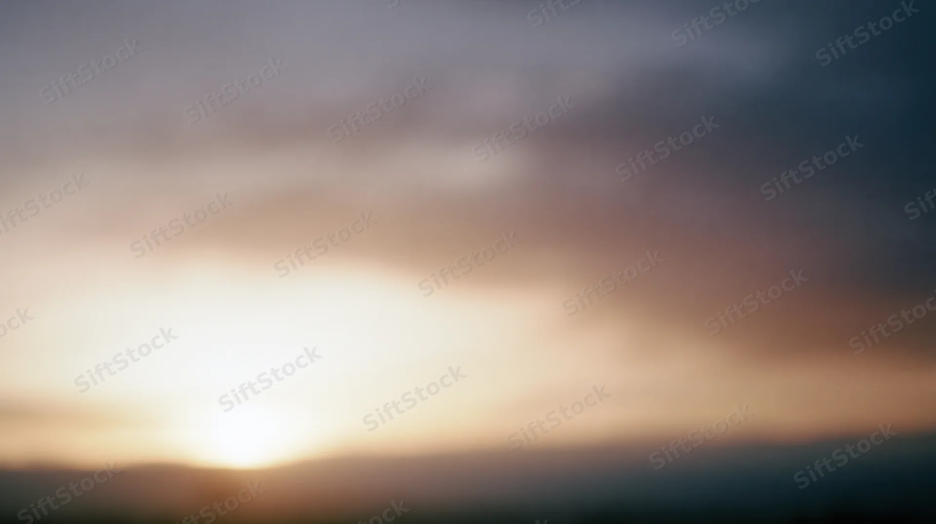 Sunset over a hazy horizon with soft clouds and warm light blending into the sky