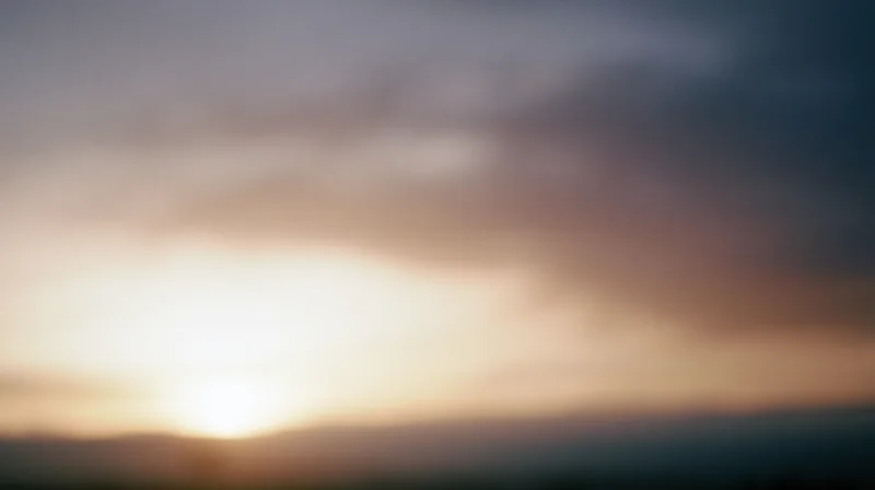 Sunset over a hazy horizon with soft clouds and warm light blending into the sky