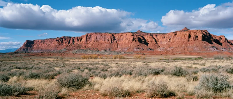 Red rock butte formation rising over arid scrubland under blue sky with clouds