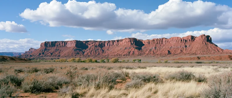 Red rock butte formation rising over arid desert plain under blue sky with clouds