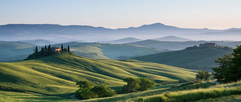 Rolling green hills with villas and cypress trees in tuscany at sunrise