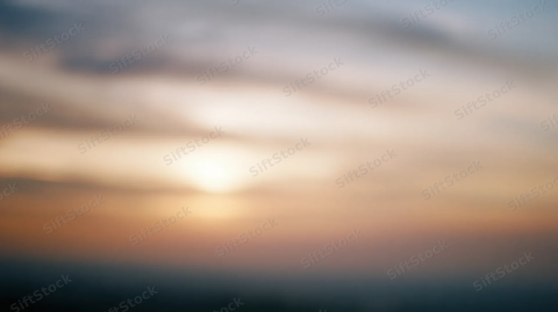 Blurred sky at sunset with soft clouds and warm light gradient across horizon