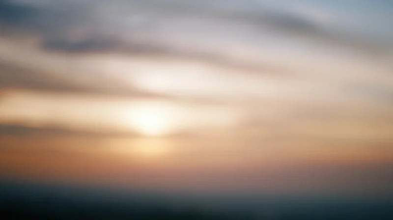 Blurred sky at sunset with soft clouds and warm light gradient across horizon