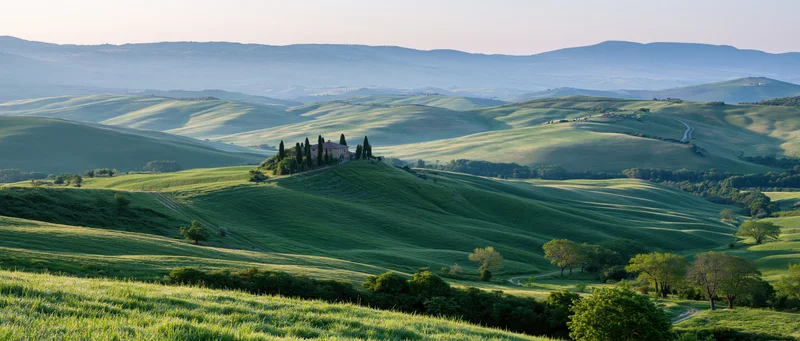 A villa surrounded by cypress trees on a green hill in the tuscan countryside at morning light