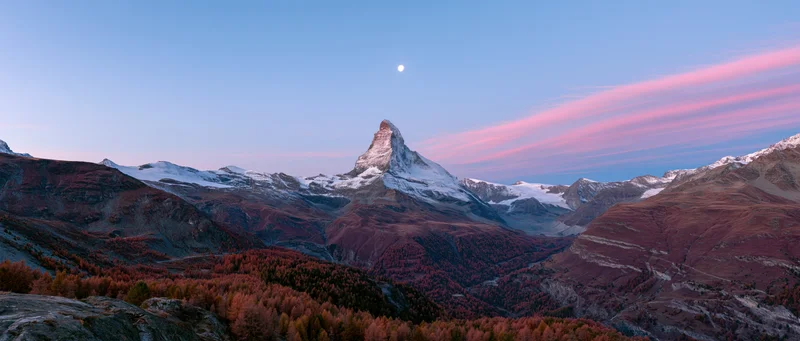 Matterhorn mountain peak covered in snow rising above autumn forested valley at twilight