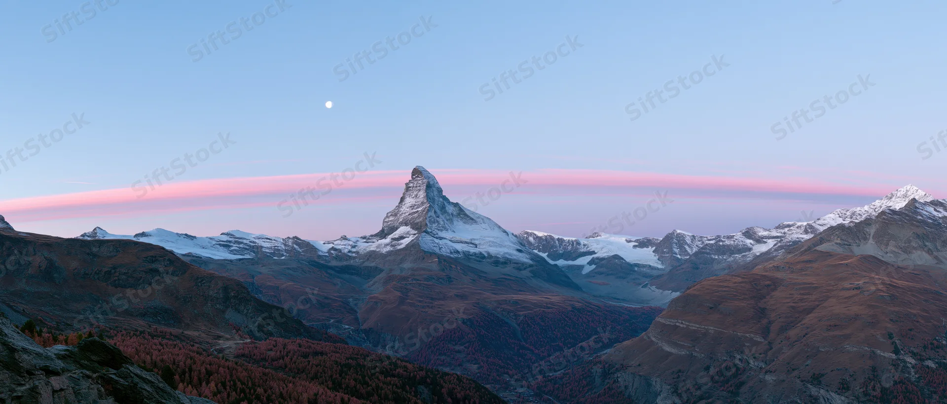 Matterhorn mountain peak at twilight with snow and autumn forest in alpine valley